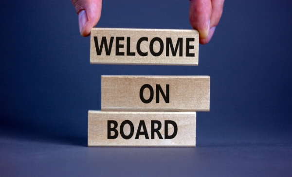 Welcome on board sign made of wooden blocks with hands arranging blocks on blue background.